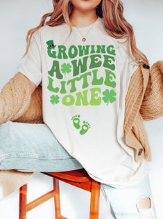 "🍀👣 This \"Growing a wee little one\" shirt is the perfect shirt for expectant mothers celebrating St. Patrick's Day! It's showcases your pregnancy in style, with a fun and festive St. Patrick's day design to make you stand out in the crowd or in your social media pictures 😉 Whether you're out and about at a parade or party, or just relaxing at home, this shirt is sure to keep you feeling great all day long since its super soft and comfy. So what are you waiting for? Click ADD TO CART now! 👕 Green Graphic Print T-shirt For First Birthday, Green Cotton T-shirt For First Birthday, First Birthday Green Top With Letter Print, Green T-shirt With Letter Print For First Birthday, Green Short Sleeve Top For First Birthday, Retro St Patricks Day, Pregnancy Gender, Pregnancy Gender Reveal, St. Patricks Day