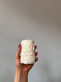 a hand holding a white candle in front of a gray wall with the light shining on it