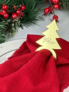 a red napkin with a gold christmas tree on it and the word merry written on it