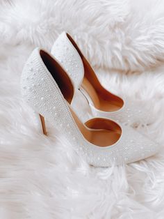 a pair of white high heeled shoes sitting on top of a fluffy white blanket