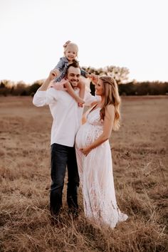 a man and woman holding a baby while standing in the middle of an open field