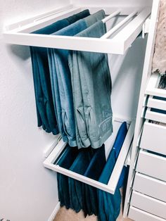 an organized closet with folded blue towels and pants hanging on the rails, in front of a white wall