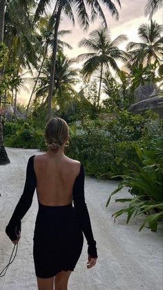 a woman in a black dress walking her dog on a path with palm trees behind her