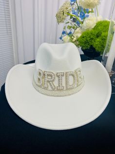 a white brimmed hat with the word bride on it sits next to a bouquet of flowers