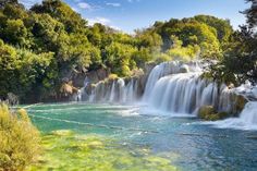 the waterfall is surrounded by green trees and clear blue water, as well as many other waterfalls