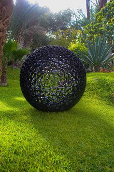 a large black ball sitting on top of a lush green field next to palm trees