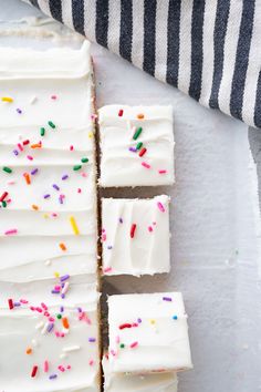 white frosted cake with colorful sprinkles on it next to a striped towel