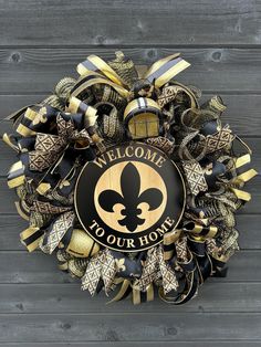 a welcome to your home wreath on a wooden wall with black and gold ribbon around it