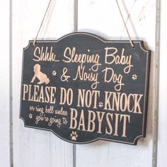 a black sign hanging on the side of a white wooden door that says, sub sleeping baby & noisy dog please do not knock our babies