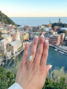 a woman's hand with a diamond ring on top of her finger in front of the ocean