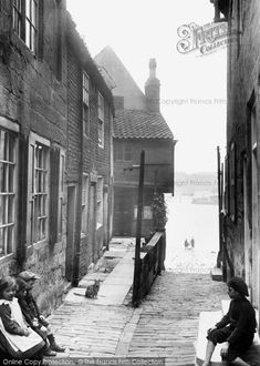 an old photo of people sitting on benches in the alleyway between two brick buildings