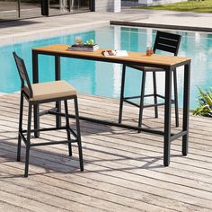 two stools sitting next to a table near a pool with a book on it