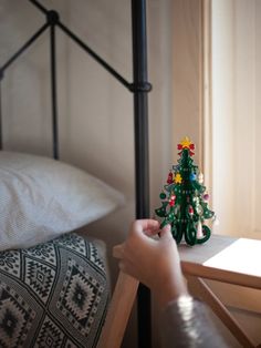 a small green christmas tree sitting on top of a wooden table next to a bed