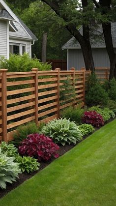 a wooden fence in front of a house surrounded by plants and flowers on the lawn