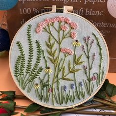 a close up of a embroidery on a table with flowers and plants in the background