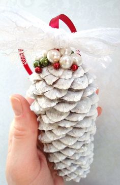 a hand holding a white pine cone ornament with pearls and bows on it