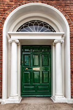 a green door with two white pillars and an arched glass window above it is on the side of a brick building