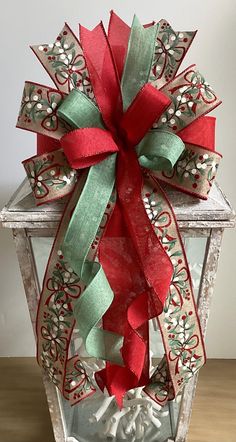 a red and green christmas bow on top of a lantern with ornaments around the edges