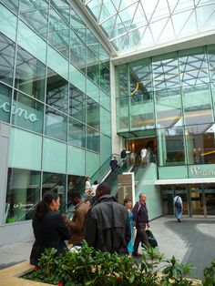 people are walking in front of a building with glass walls and stairs that lead up to the second floor