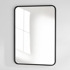 a white wall with a black frame and a mirror on it's side that is reflecting the light coming in