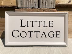 a sign that says little cottage in black ink on a white background with wood planks behind it