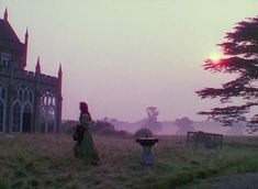 a woman standing on top of a lush green field next to a tall church tower