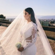 a woman in a white wedding dress and veil standing on a roof with a city view behind her