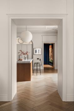 an open door leading to a kitchen and dining room with white walls, wood floors and parquet flooring