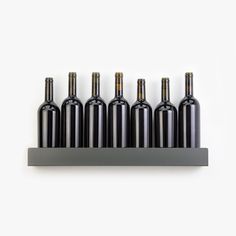 six wine bottles are lined up in a row on a metal shelf against a white wall