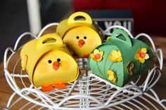 three little yellow chicks are sitting in a wire basket on top of a wooden table