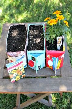 three planters sitting on top of a wooden table filled with dirt and flowers next to each other