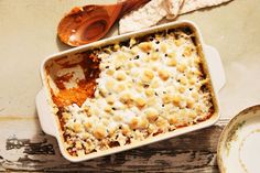 a casserole dish filled with pasta and sauce next to a wooden spoon on a table