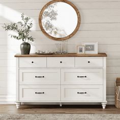 a white dresser with drawers and a round mirror on the wall next to a basket