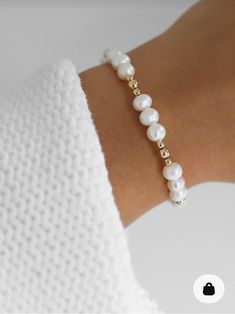 a woman's arm wearing a bracelet with white pearls and gold beads on it