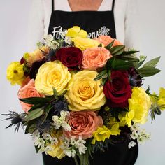 a woman wearing an apron holding a bouquet of roses and other flowers in her hands