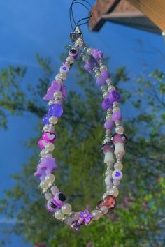 a close up of a beaded necklace hanging from a tree with trees in the background