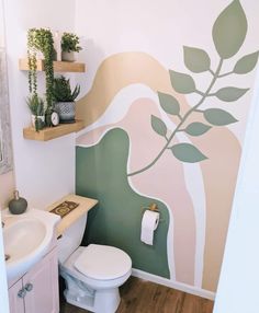 a bathroom with a toilet, sink and green plant wall decal on the wall