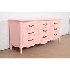 an old pink dresser with gold handles and knobs on the drawers is against a white brick wall