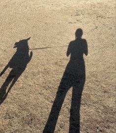 the shadow of two people and a dog in an open field with no one on it