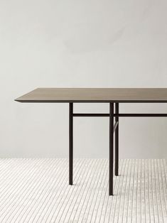 a rectangular table with two black legs and a wooden top on a white floor in front of a wall