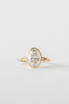 a yellow gold ring with an oval cut diamond in the center, on a white background