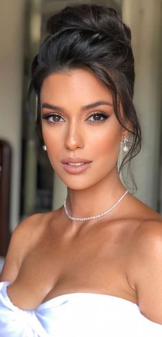 a woman in a white dress with pearls on her neck and shoulder, posing for the camera