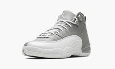 The Air Jordan 12 GS “Stealth” is the youth sizing of the retro basketball shoe in a two-tone grey and white colorway.  Originally released in 1997, the Jordan 12 was worn by Michael Jordan with the Chicago Bulls during the ‘96-97 NBA season, and in the ‘97 NBA Playoffs.  The “Stealth” honors the shoe’s 25th anniversary.  Details include a Stealth Grey tumbled leather upper paired with a white pebbled mudguard.  Metallic Silver eyelets appear on the collar, and a grey nylon pull tab is found on Gray And White Jordans, Jordan 12s, Grey Jordans, Jordan Retro 12, Retro Basketball Shoes, White Jordans, Nike Shoes Girls, Retro Basketball, Air Jordan 12