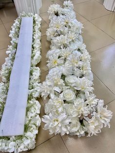 two white flowers are laying on the floor next to a long piece of cloth that has been folded over it