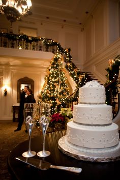 a white wedding cake sitting on top of a table next to two champagne glasses and a christmas tree