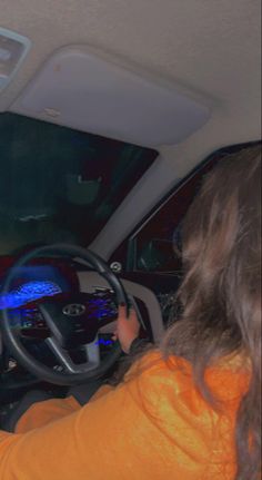 a woman driving a car while wearing an orange shirt and holding the steering wheel with both hands