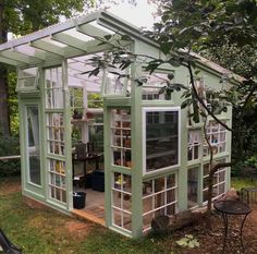 a small green house sitting in the middle of a yard with lots of windows on it