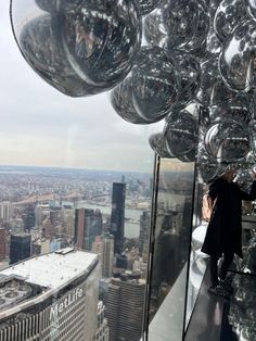 a man standing on top of a tall building next to a window filled with glass balls