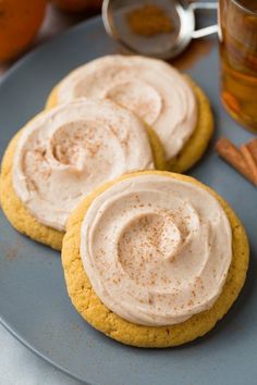 three cookies with frosting and cinnamon on a plate next to a glass of tea