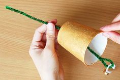 two hands are holding a paper cup with green string attached to it and another hand is holding a plastic tube